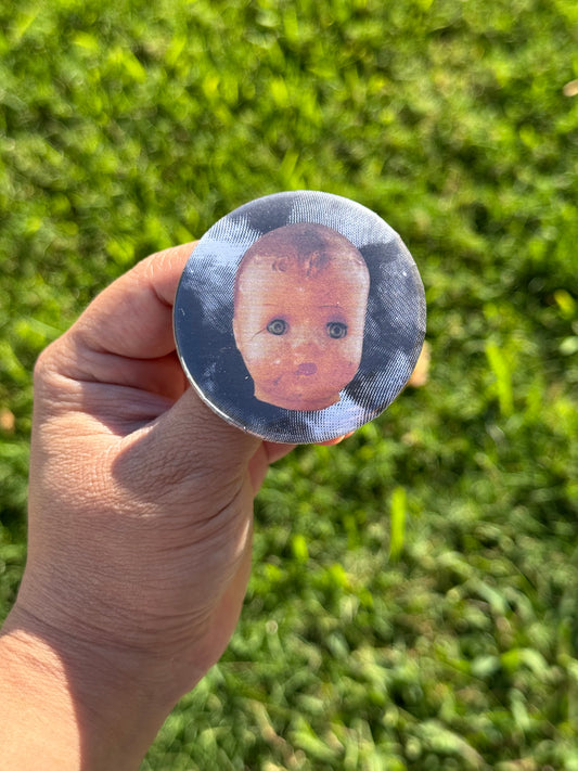 Button pin with black and white background and creepy doll head in the forefront. 