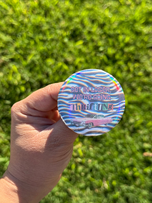 Holographic button pin zebra striped background with retro pink car and text that says “Get in loser, we’re going thrifting.” 